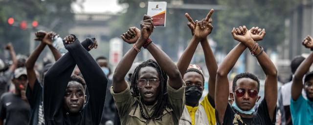 Manifestant·es, poings croisés, devant des agents de police kényans lors d’une manifestation contre la hausse des impôts dans le centre-ville de Nairobi, le 18 juin 2024, alors que les membres du Parlement débattent de la loi de finance 2024.