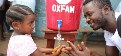 A community health worker shows a young girl how to wash her hands in Tengbeh Town, Sierra Leone, to prevent Ebola's spread. Photo: Will Wintercross/Oxfam