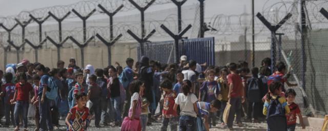 Des enfants syriens se regroupent dans le camp de réfugiés de Zaatari, en Jordanie, devant une barrière et des barbelés.