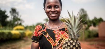 Mukeshimana Leocadie tient un ananas devant la coopérative de Tuzamurane, à l’est du Rwanda, dont elle est l’un des membres.