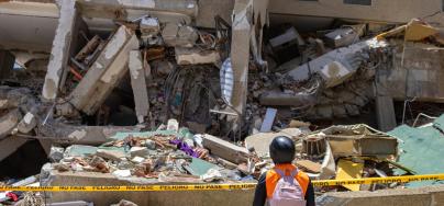 A volunteer observes a collapsed structure in the aftermath of the earthquakes. A community member surveys the damage caused by the disaster. Community efforts have been key to supporting those affected.