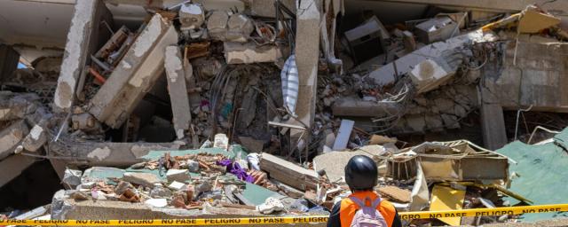 A volunteer observes a collapsed structure in the aftermath of the earthquakes. A community member surveys the damage caused by the disaster. Community efforts have been key to supporting those affected.