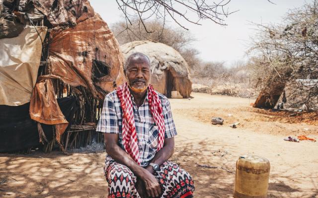 Sankuus*, 70, sits in front of the home he shared with his wife who recently passed away due to thirst.