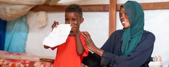 The son of Nadia Zahad, a refugee from the Sudan war, proudly displays his artwork created at a child-friendly center in Renk. The center provides a safe space for children to play and express themselves through art.