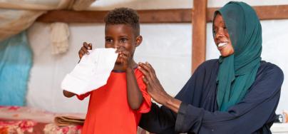 The son of Nadia Zahad, a refugee from the Sudan war, proudly displays his artwork created at a child-friendly center in Renk. The center provides a safe space for children to play and express themselves through art.
