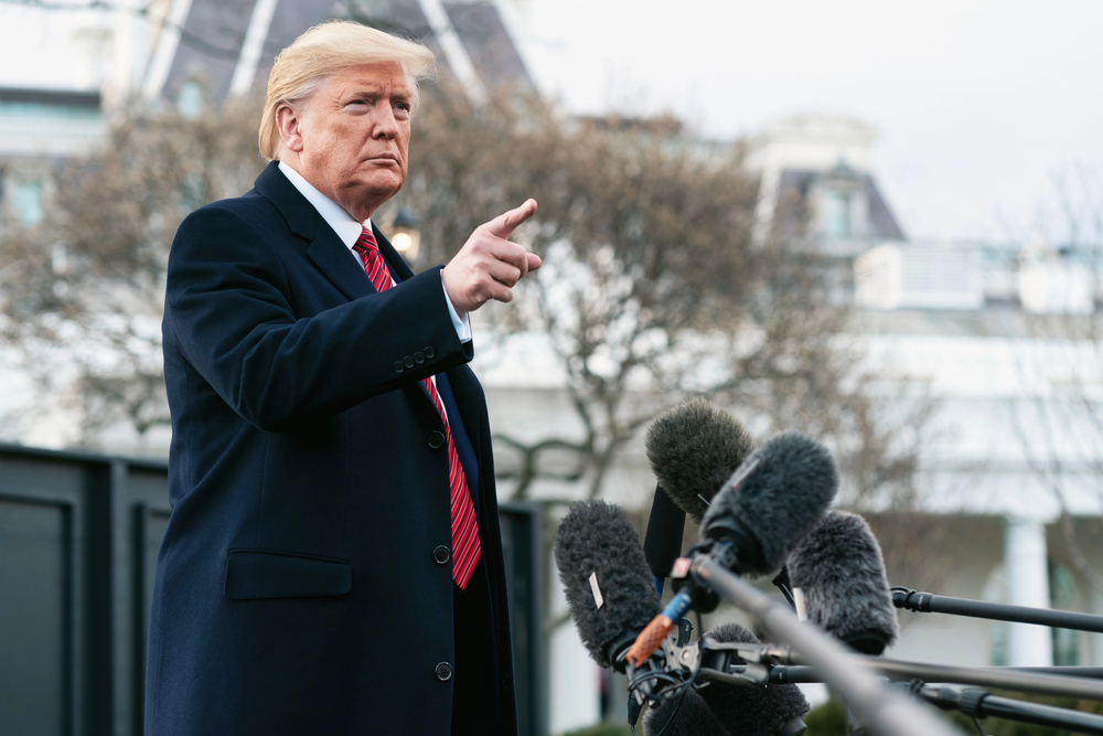 President Donald Trump speaking to members of the press with many microphones in front of him, pointing and fielding questions — Photo by Tennessee